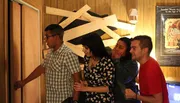 A group of individuals appears engaged and possibly intrigued or anxious, as one person opens a door that is part of a barricaded wooden structure, while others look on with anticipation.