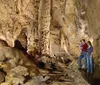 Visitors are exploring a naturally illuminated cave with a clear pool of water and intriguing rock formations