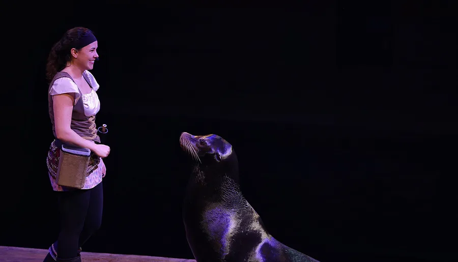 A woman is smiling at a sea lion in a dimly lit setting.